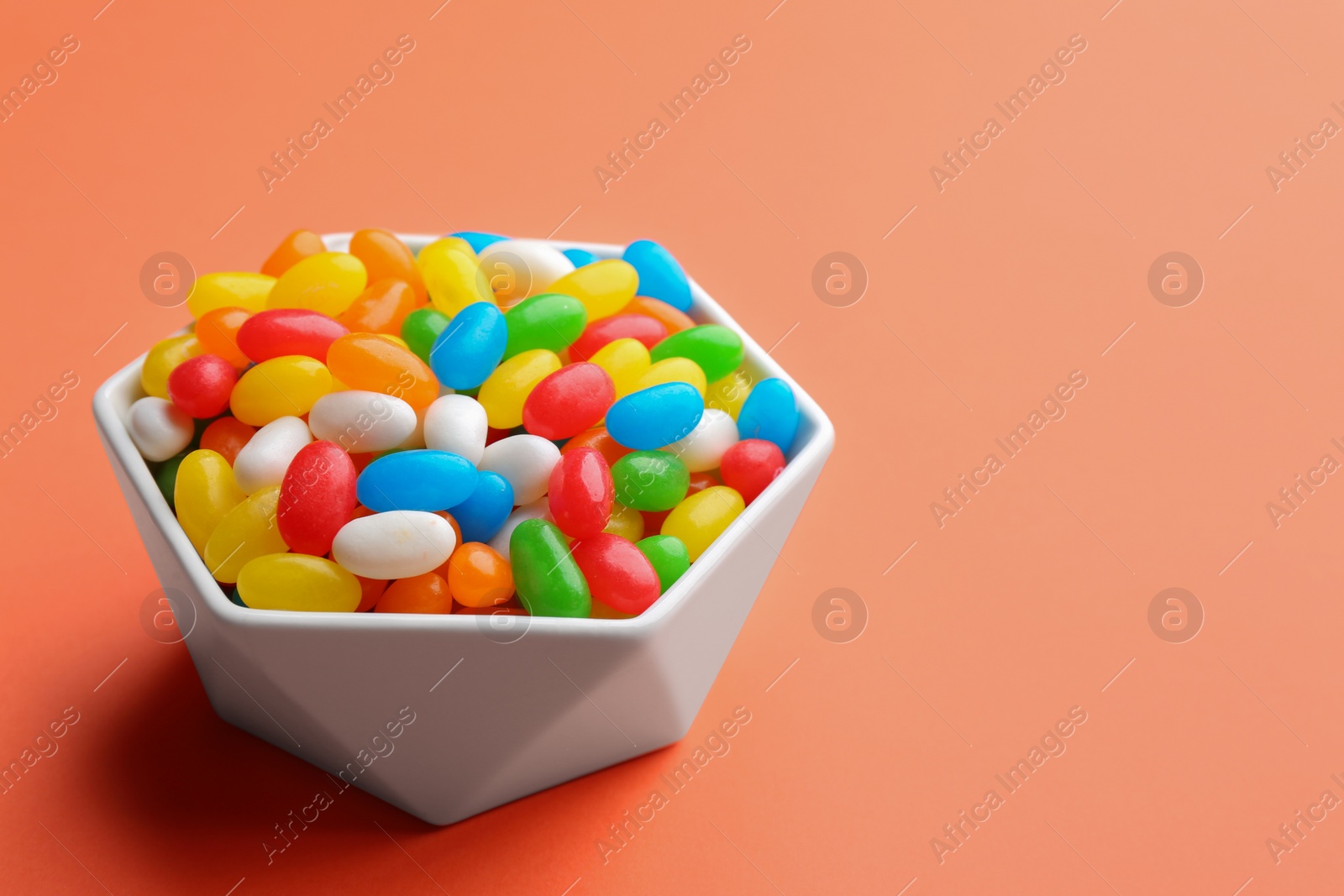 Photo of Bowl with colorful jelly beans on coral background. Space for text