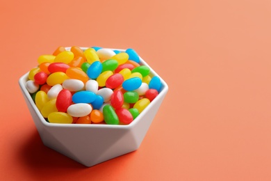 Bowl with colorful jelly beans on coral background. Space for text