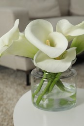 Beautiful calla lily flowers in glass vase on white table indoors