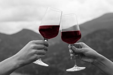 Friends clinking glasses of wine in mountains, closeup. Black and white photo with red accent