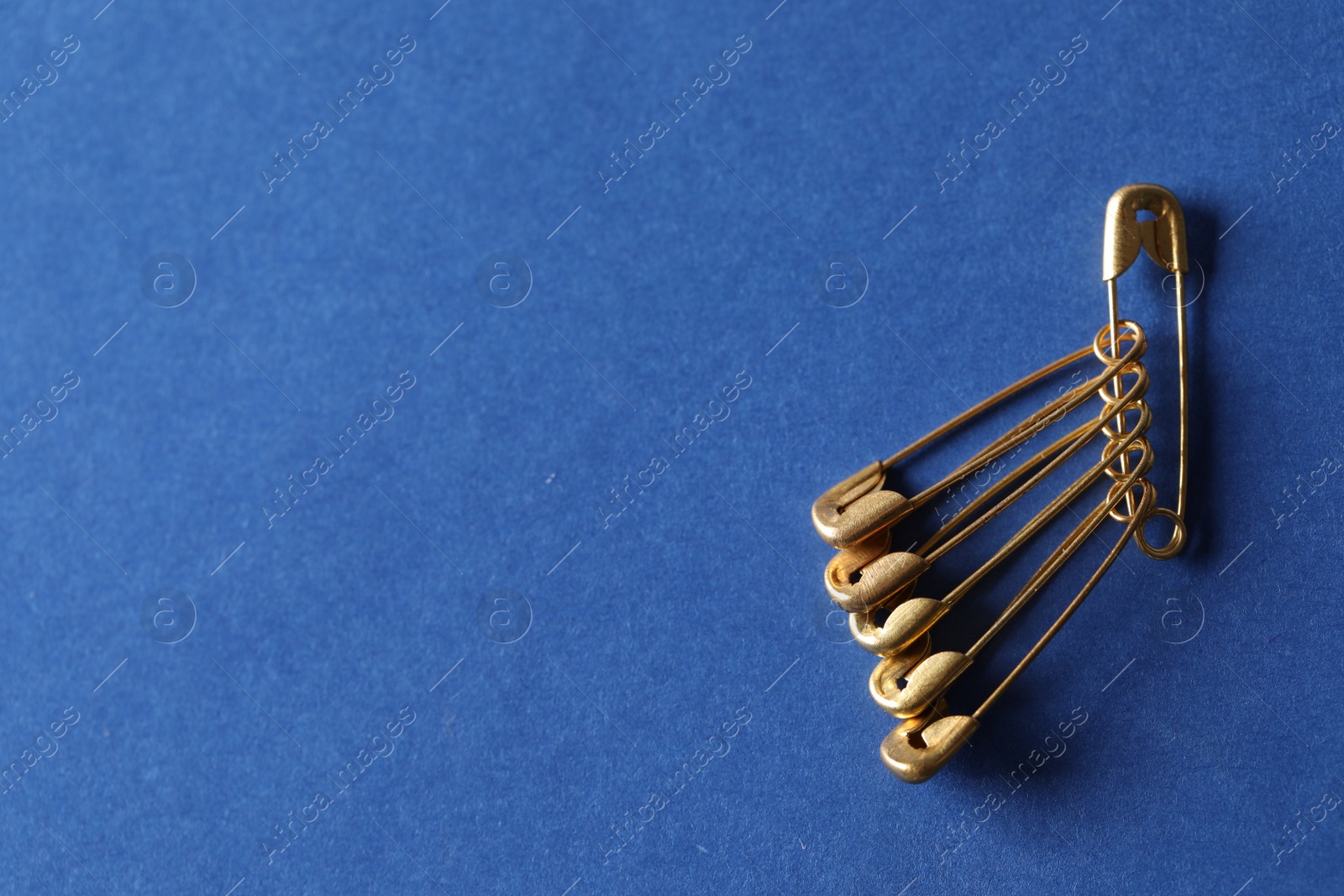 Photo of Golden safety pins on blue background, flat lay. Space for text