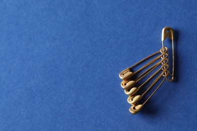 Photo of Golden safety pins on blue background, flat lay. Space for text