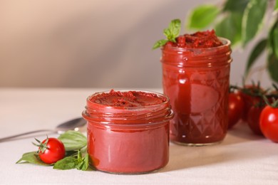 Photo of Jars of tasty tomato paste and ingredients on white table, closeup. Space for text