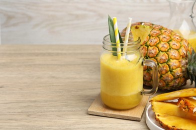 Tasty pineapple smoothie and fruit on wooden table. Space for text