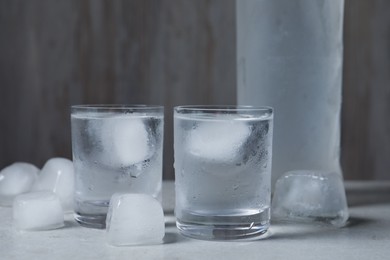 Photo of Shot glasses and bottle of vodka with ice cubes on light grey table