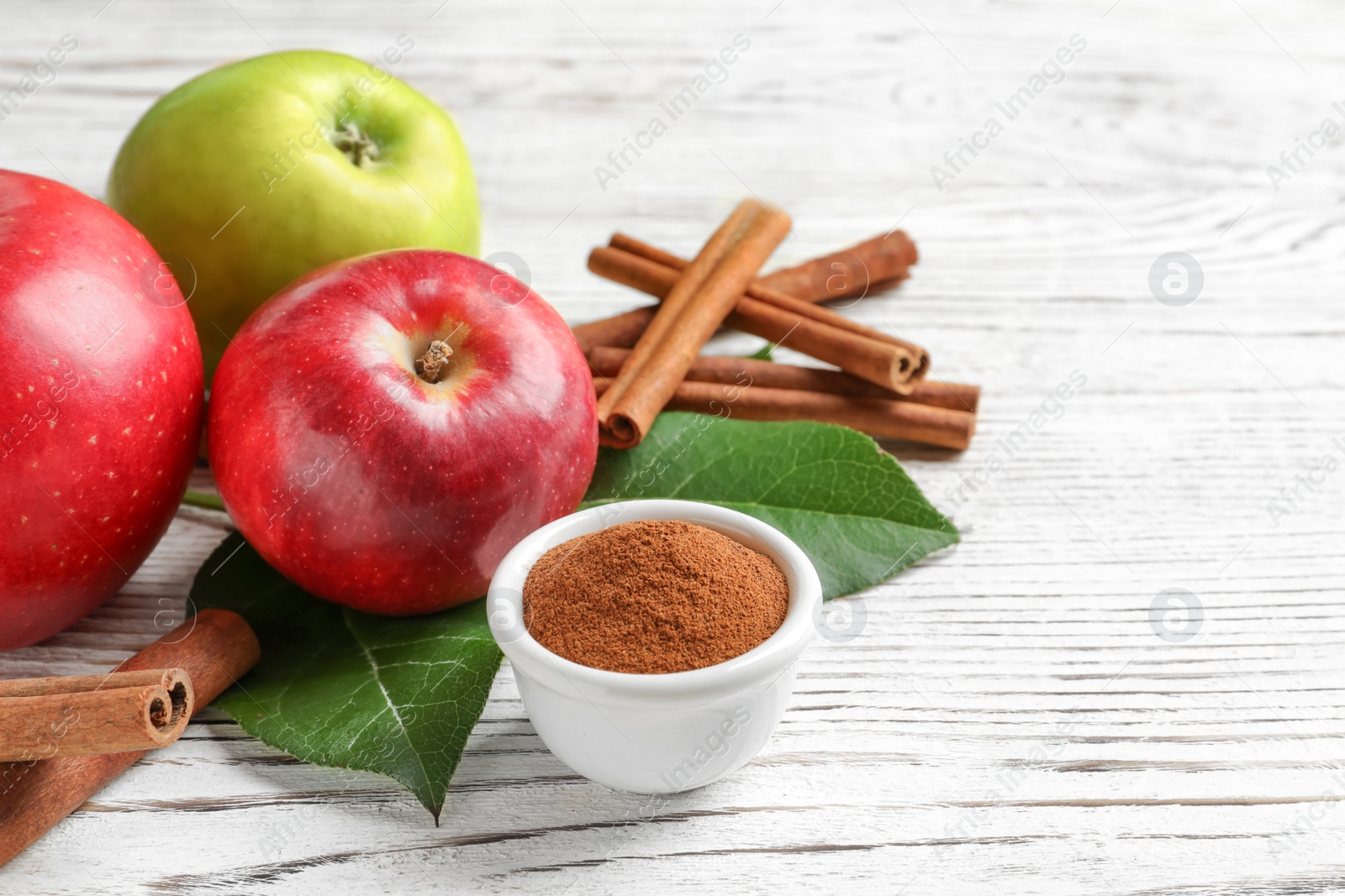 Photo of Fresh apples with cinnamon sticks and powder on wooden table