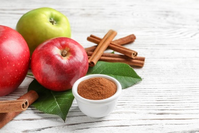 Fresh apples with cinnamon sticks and powder on wooden table