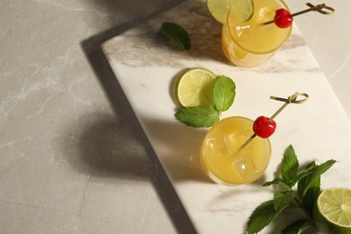Photo of Glasses of tasty pineapple cocktail decorated with cherry and lime on light grey marble table, top view. Space for text