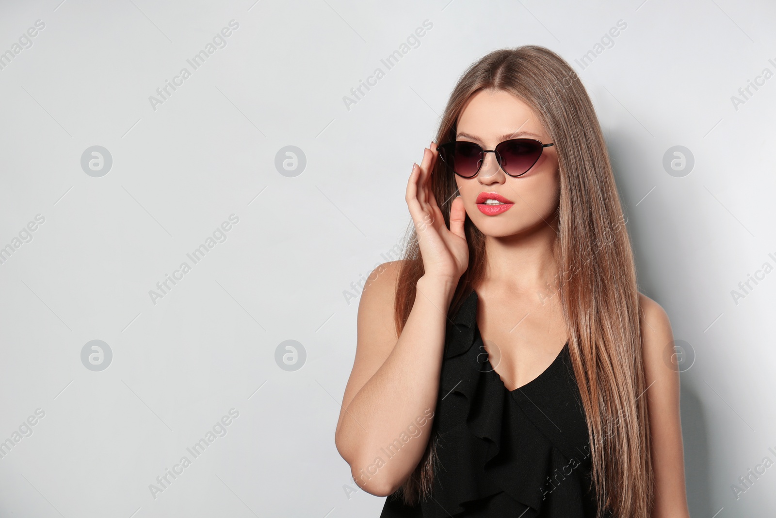 Photo of Young woman wearing stylish sunglasses on light background. Space for text