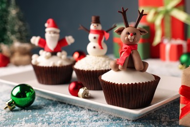 Different beautiful Christmas cupcakes on blue table with festive decor and snow