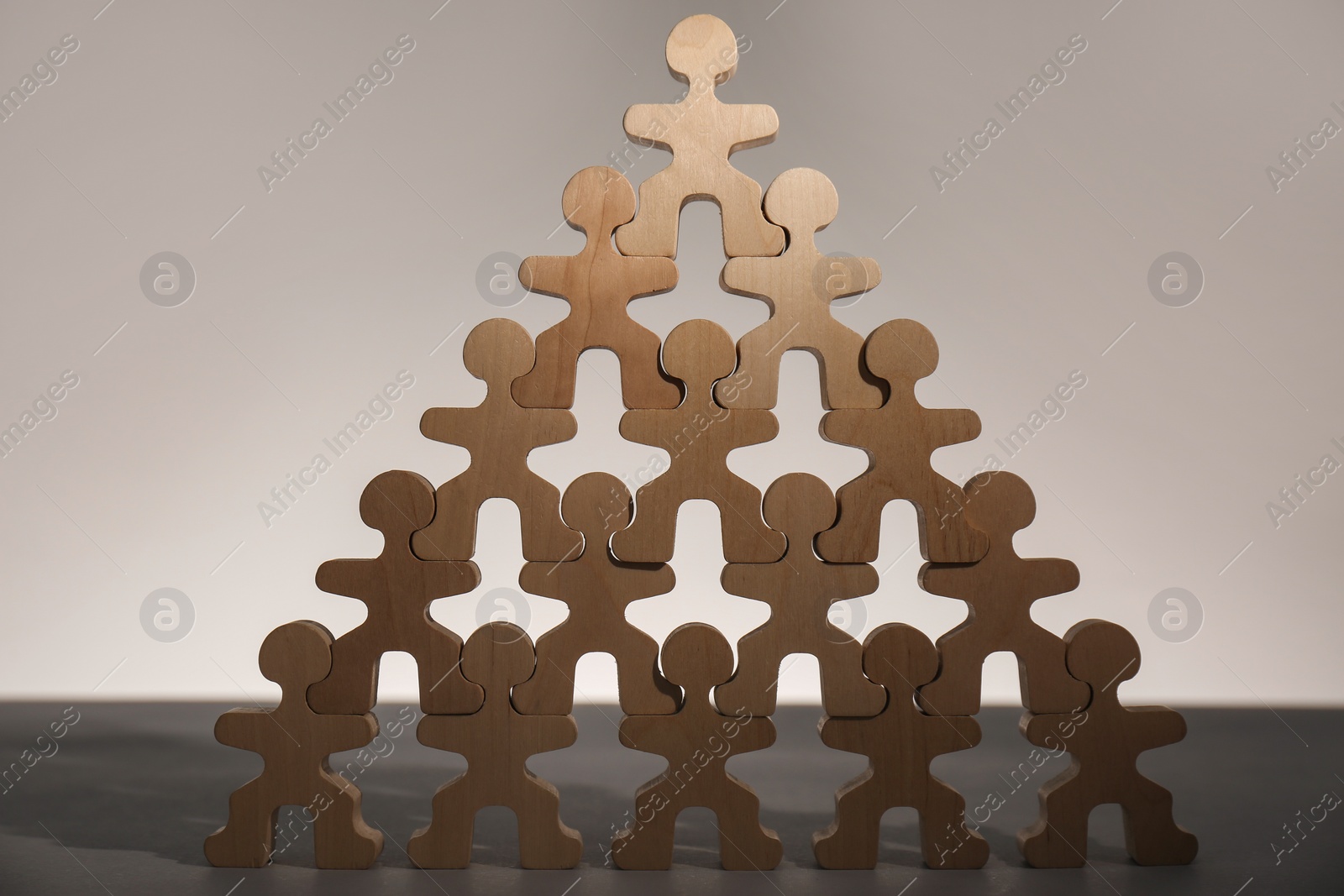 Photo of Recruitment process, job competition concept. Pyramid of wooden human figures with noticeable one on top as prime applicant on grey table