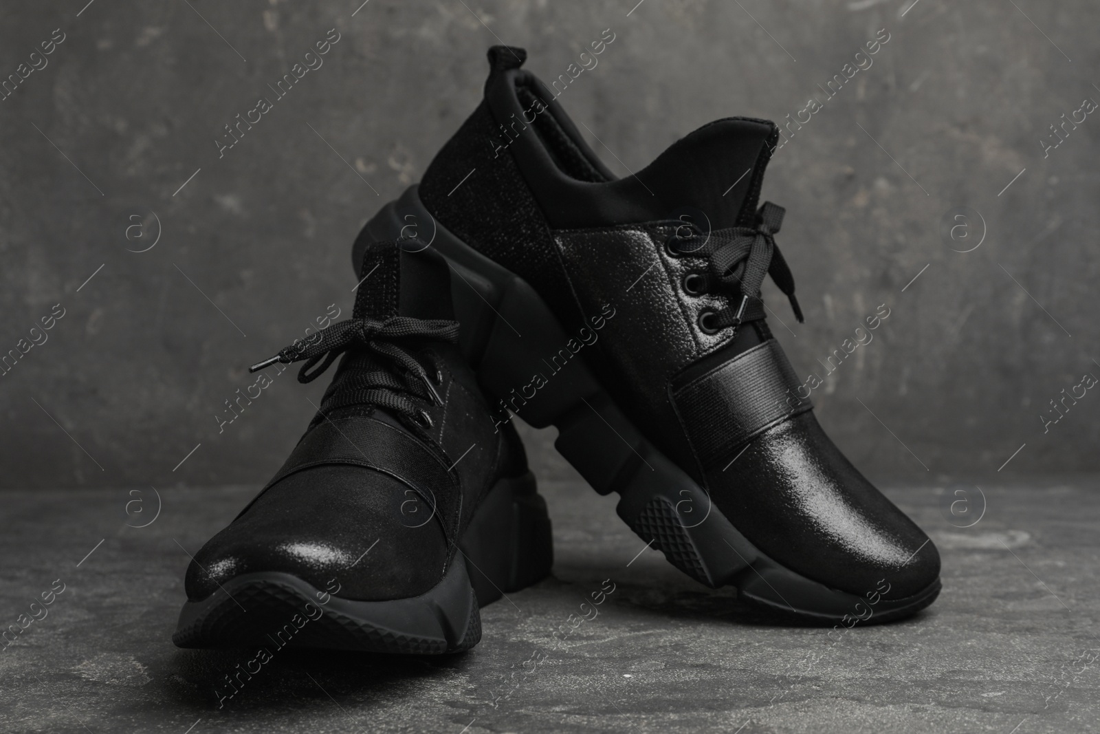 Photo of Stylish black sneakers on grey stone table, closeup