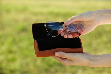 Woman holding sunglasses and case outdoors on sunny day, closeup