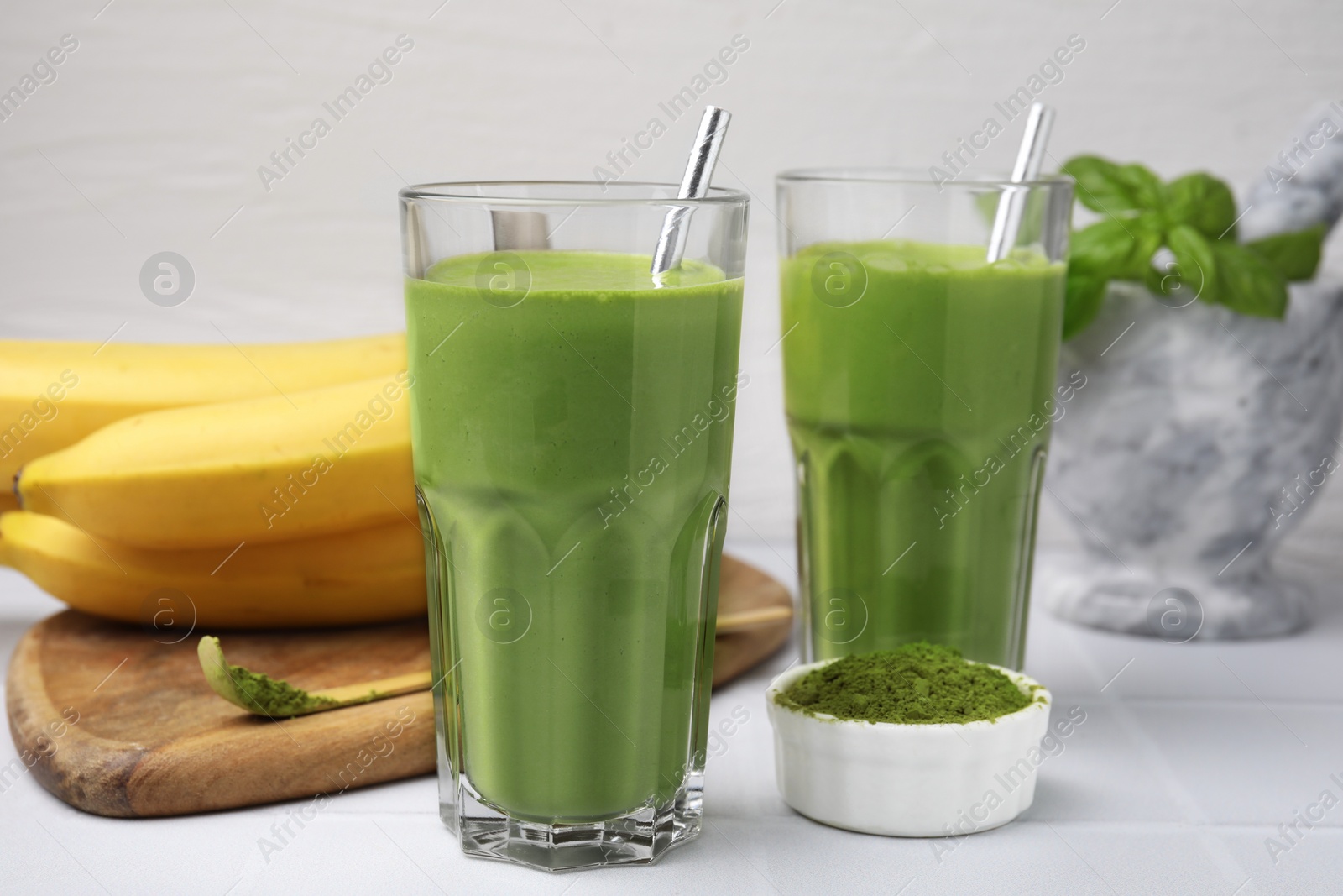 Photo of Glasses of tasty matcha smoothie and powder on white table