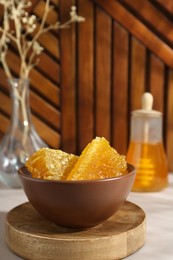 Photo of Natural honeycombs and honey in bowl on white table, space for text
