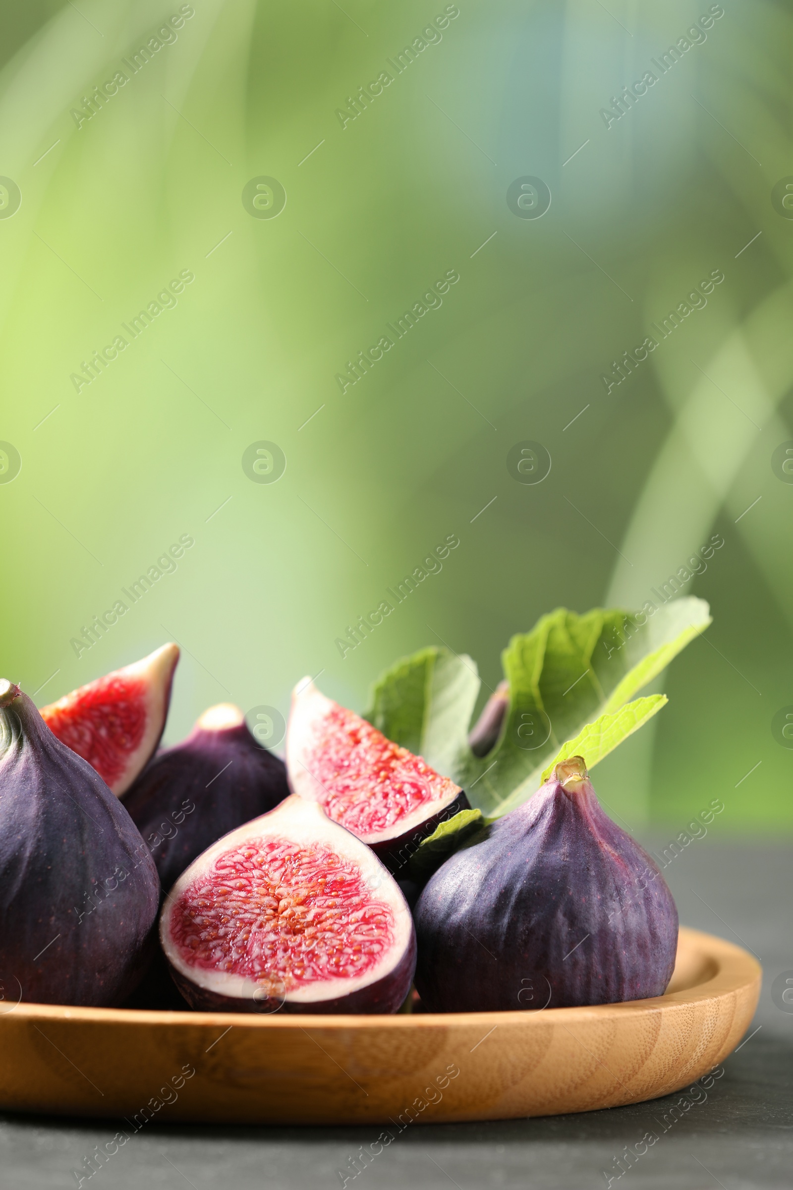 Photo of Plate with fresh ripe figs and green leaf on grey table. Space for text