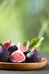 Photo of Plate with fresh ripe figs and green leaf on grey table. Space for text