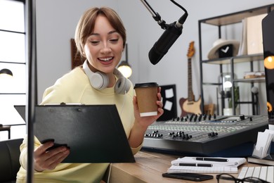 Woman with cup of coffee working as radio host in modern studio