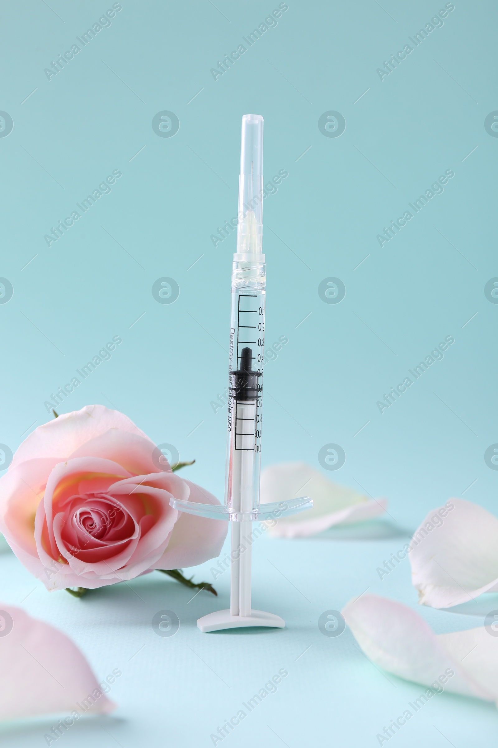 Photo of Cosmetology. Medical syringe, rose flower and petals on light blue background