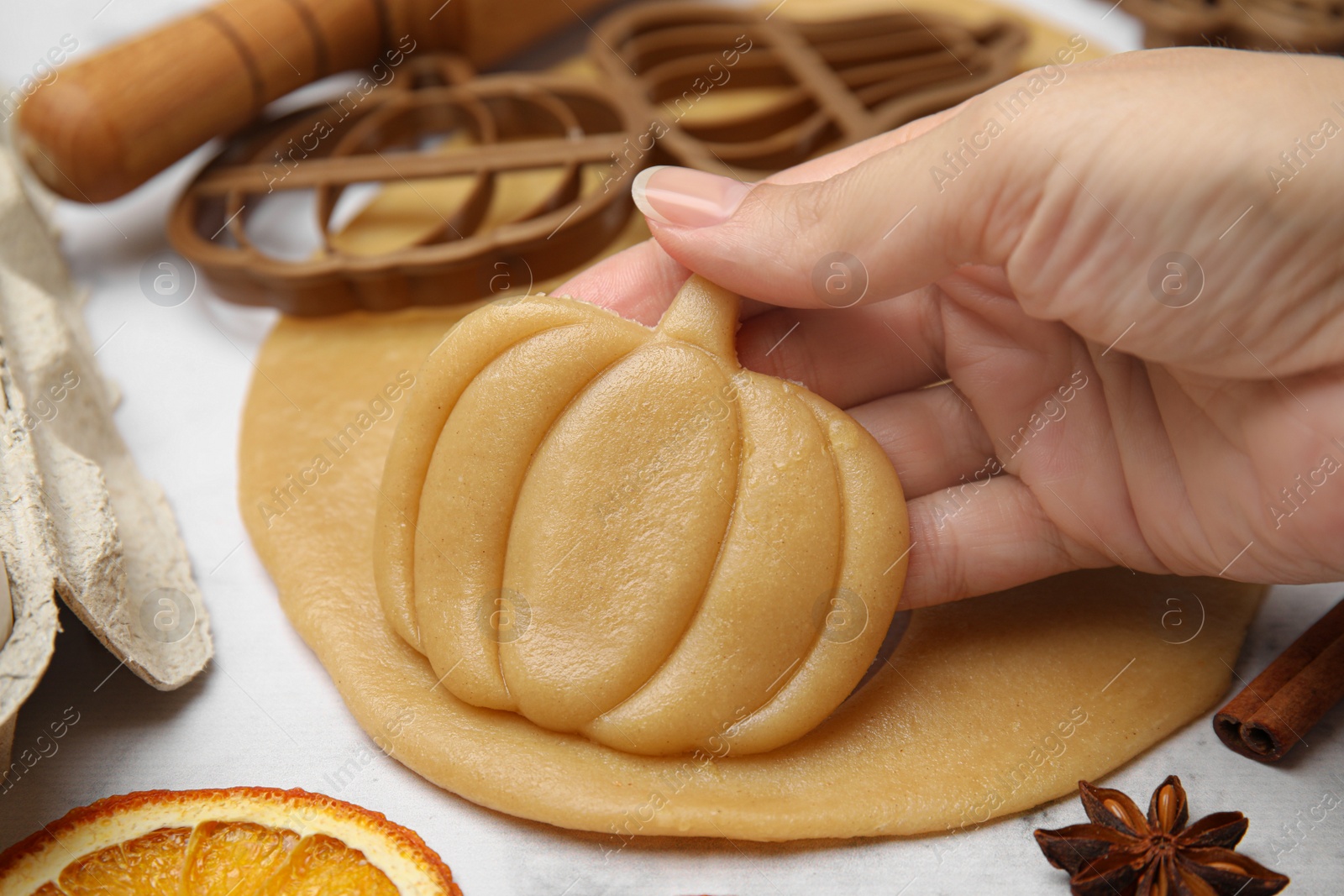 Photo of Woman holding unbaked pumpkin shaped cookie at white table, closeup