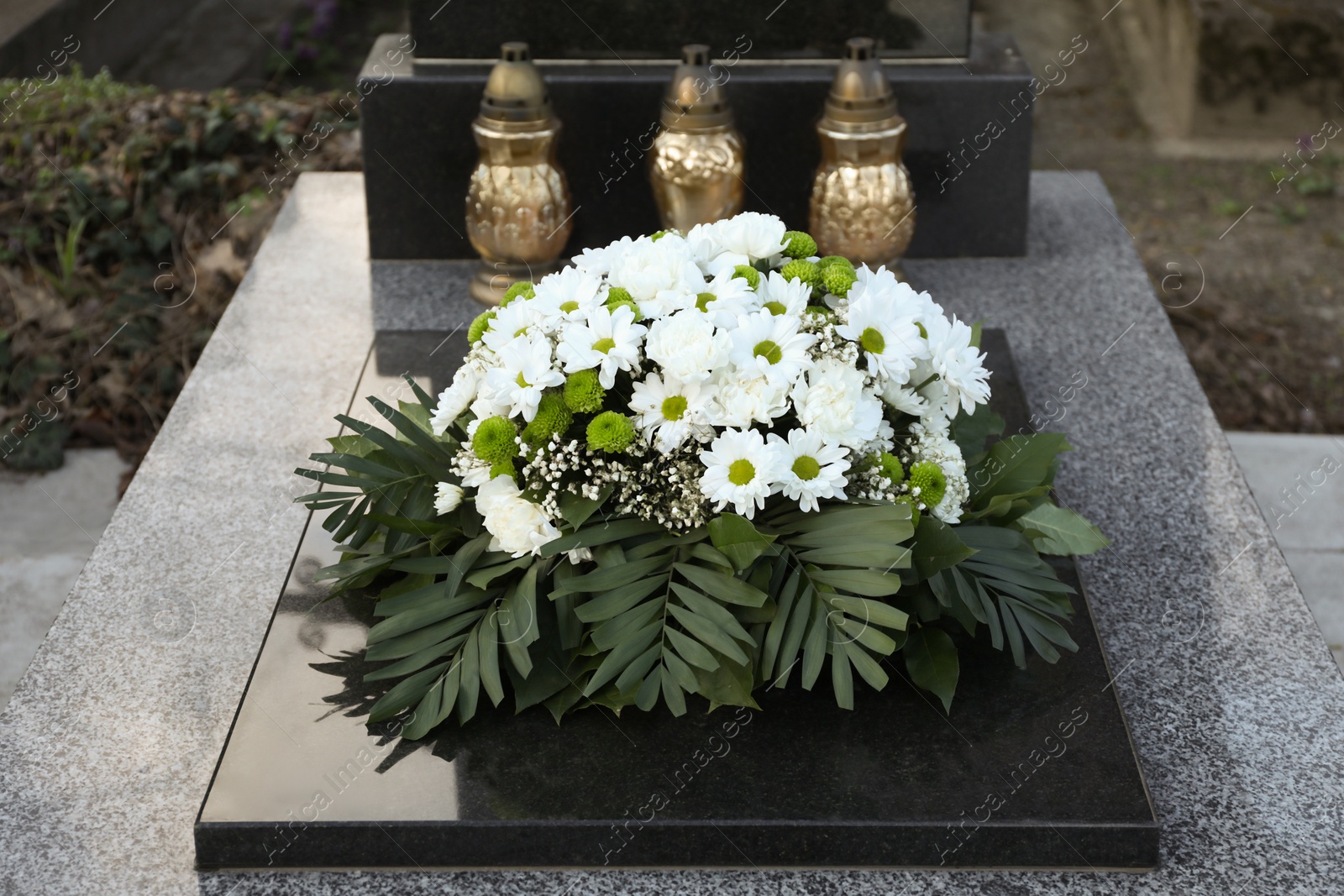 Photo of Funeral wreath of flowers and grave lanterns on granite tombstone in cemetery