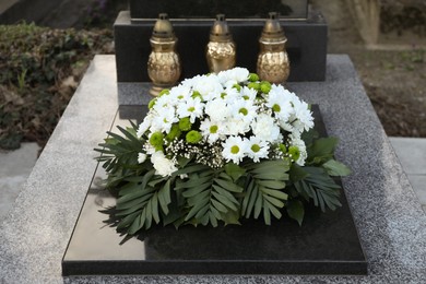 Funeral wreath of flowers and grave lanterns on granite tombstone in cemetery