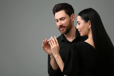 Man putting elegant ring on woman's finger against dark grey background. Space for text