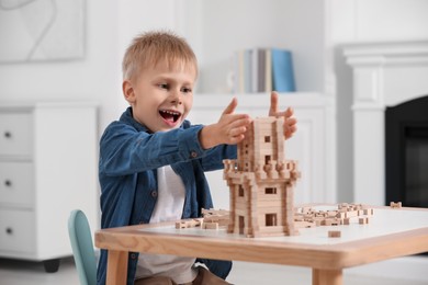 Cute little boy playing with wooden tower at table indoors. Child's toy