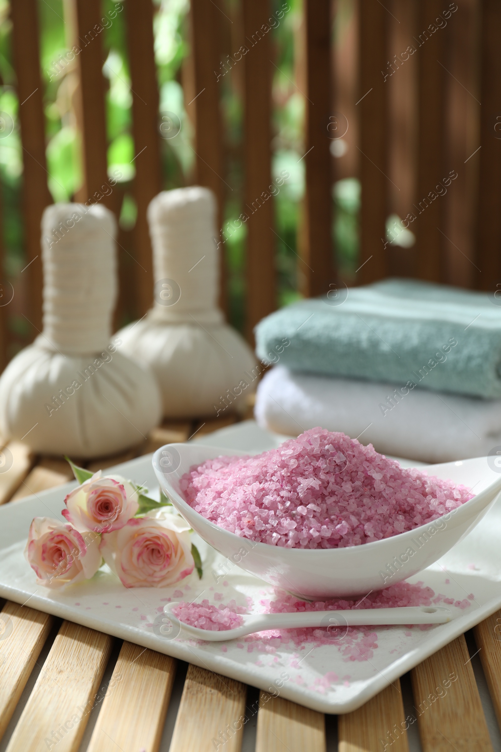 Photo of Bowl of pink sea salt and beautiful roses on wooden table, space for text