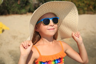 Little girl in stylish sunglasses and hat on beach