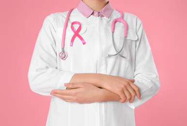 Photo of Doctor with pink ribbon and stethoscope on color background, closeup. Breast cancer awareness