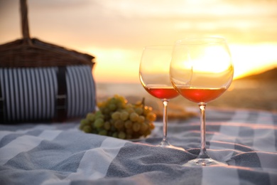 Photo of Blanket with glasses of wine and food on beach at sunset. Romantic picnic for couple