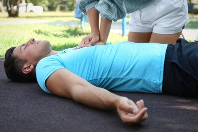 Photo of Young woman performing CPR on unconscious man outdoors. First aid