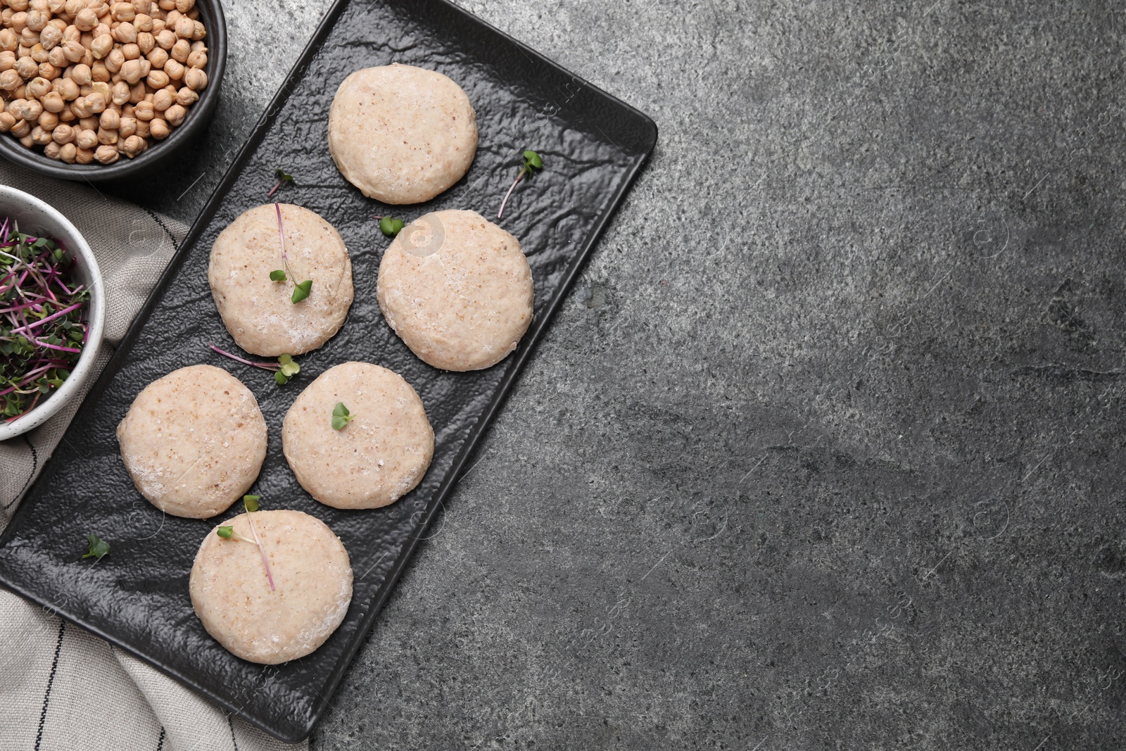 Photo of Raw vegan nuggets, greens and chickpeas on grey table, flat lay. Space for text