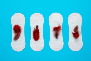 Photo of Menstrual pads with red feathers on light blue background, flat lay
