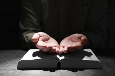 Photo of Religion. Christian man praying over Bible at table, closeup