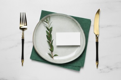 Photo of Stylish setting with cutlery, eucalyptus leaves and blank card on white marble table, flat lay. Space for text