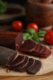 Photo of Delicious dry-cured beef basturma with basil and tomatoes on wooden table, closeup
