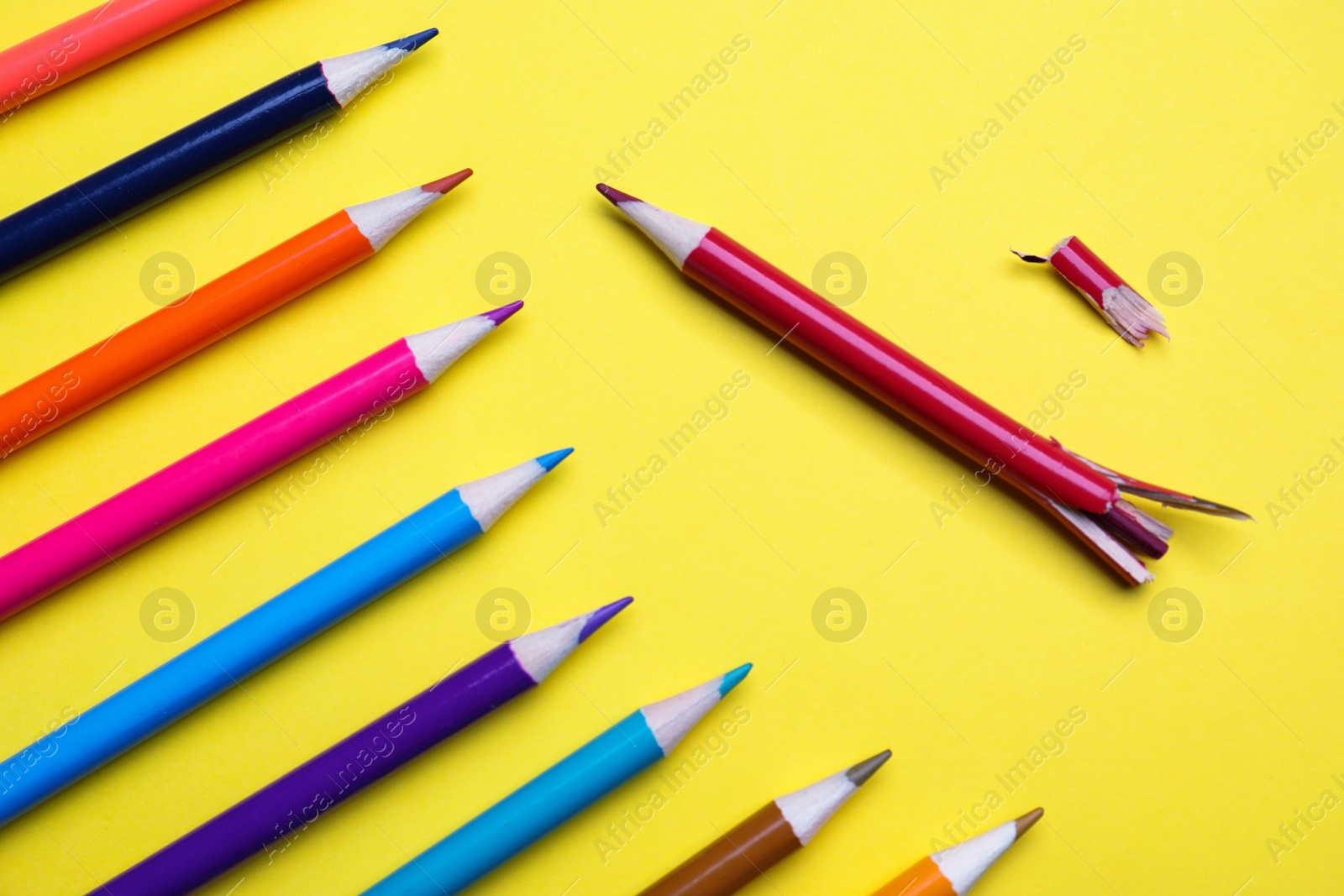 Photo of Whole colorful pencils and broken one on yellow background, flat lay. Bullying concept