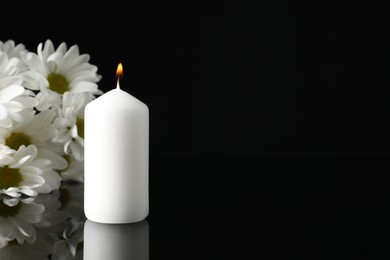 Photo of Burning candle and white chrysanthemum flowers on black mirror surface in darkness, space for text. Funeral symbols