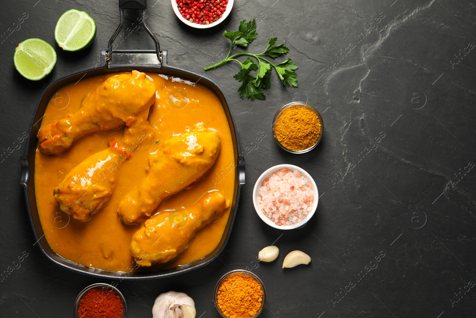 Photo of Tasty chicken curry and ingredients on black textured table, flat lay. Space for text