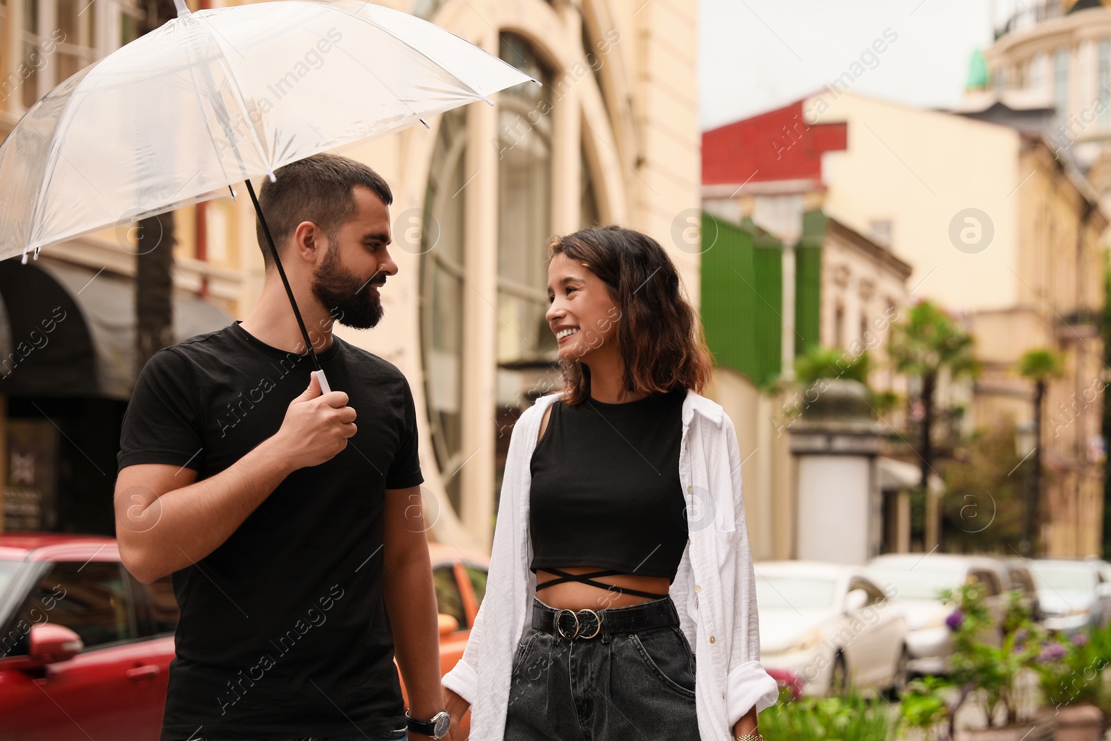 Photo of Young couple with umbrella enjoying time together under rain on city street