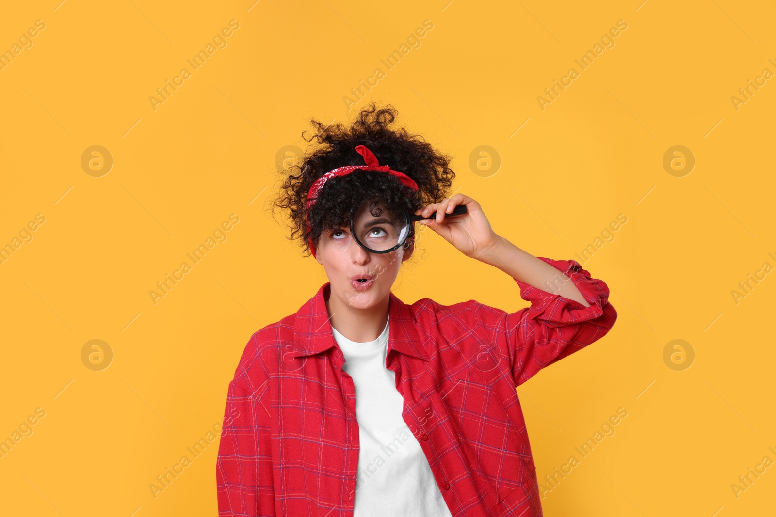 Photo of Curious young woman looking through magnifier glass on yellow background