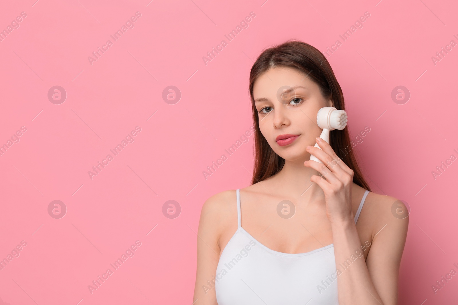 Photo of Washing face. Young woman with cleansing brush on pink background, space for text