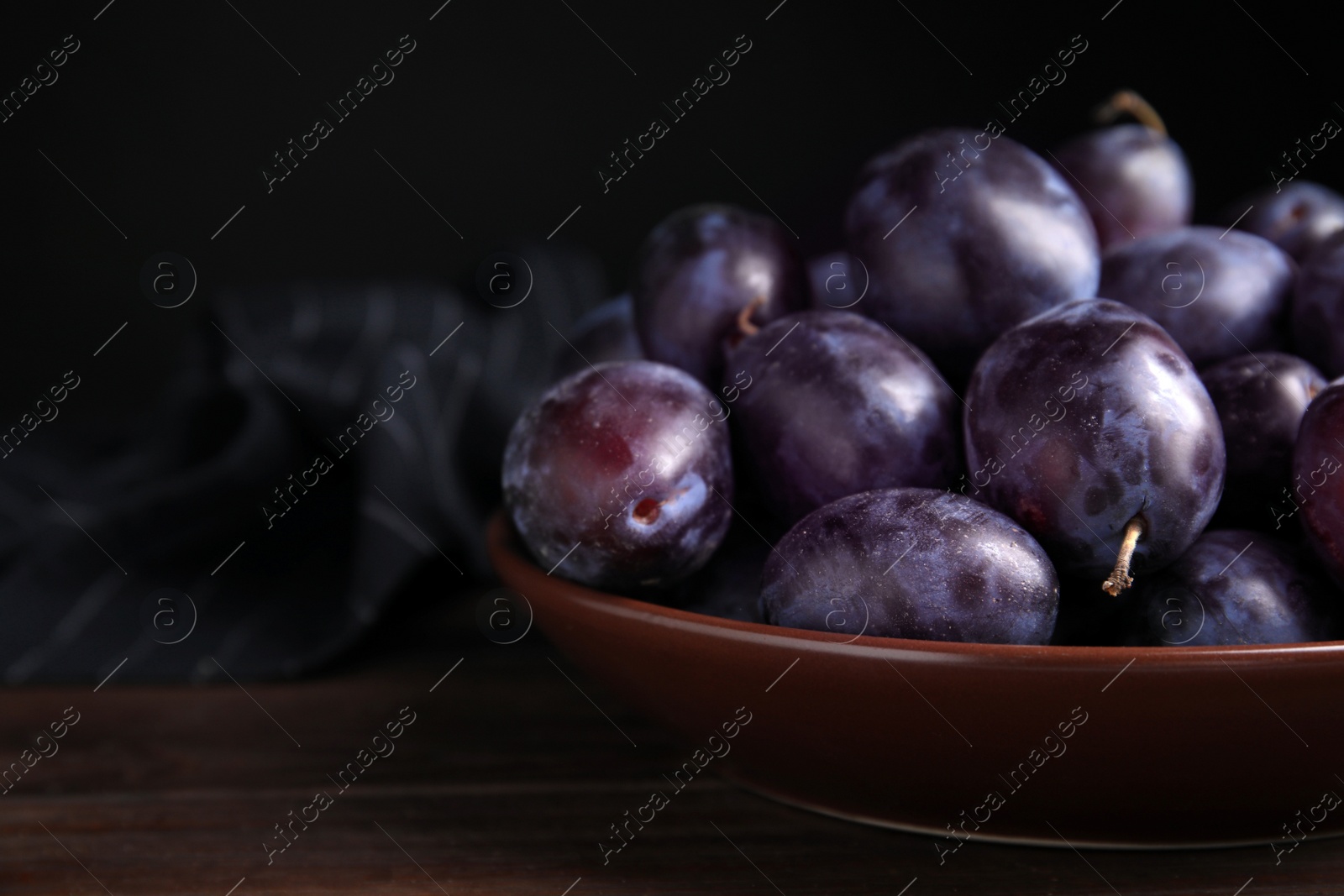 Photo of Delicious ripe plums in bowl on wooden table, space for text