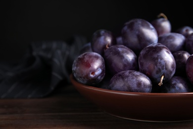 Delicious ripe plums in bowl on wooden table, space for text