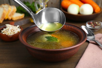 Photo of Pouring delicious chicken bouillon into bowl on wooden table, closeup
