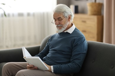 Photo of Portrait of happy grandpa reading book on sofa indoors