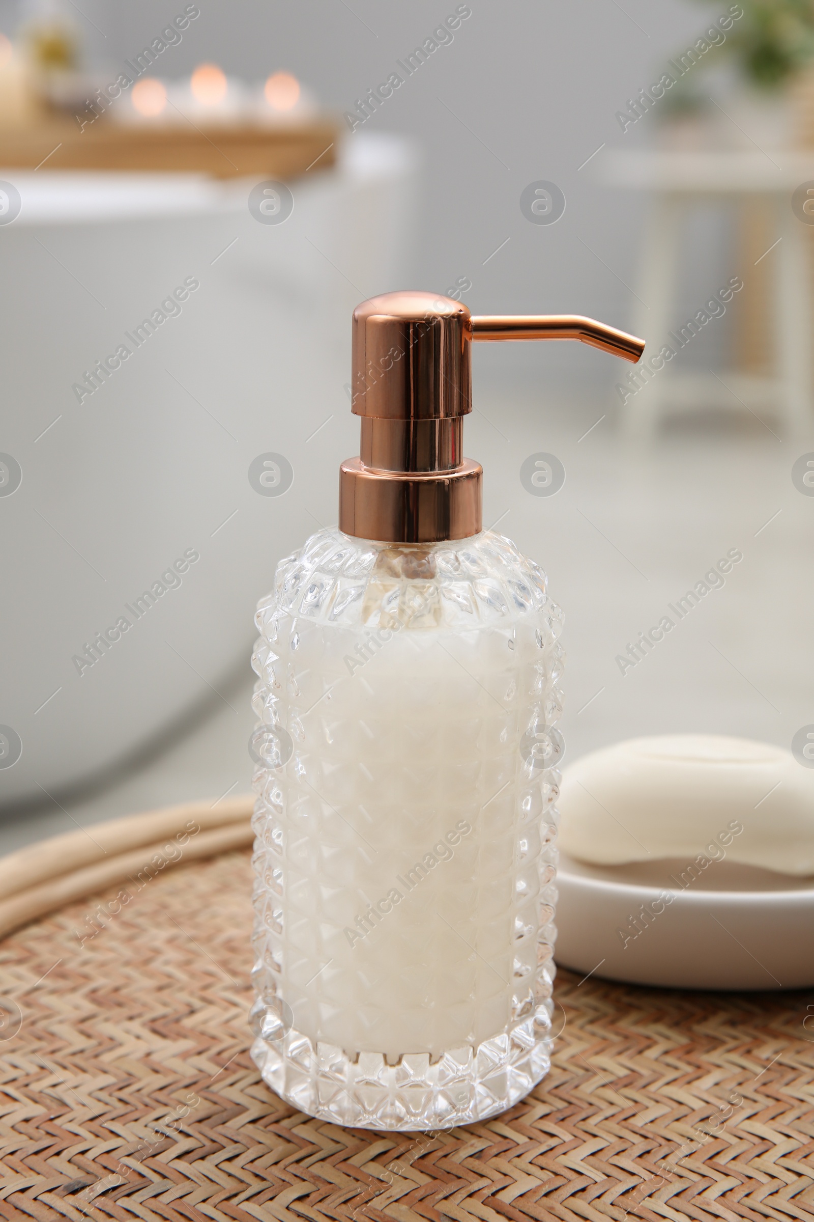 Photo of Stylish glass dispenser and soap bar on wicker stool in bathroom