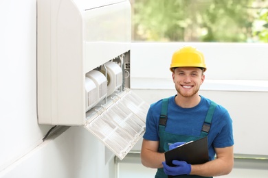 Professional technician with clipboard near modern air conditioner indoors